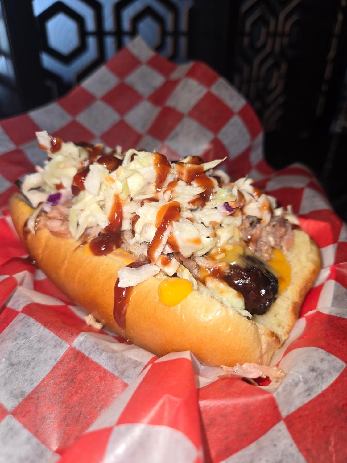 Coney dog topped with coleslaw, cheese and BBQ sauce